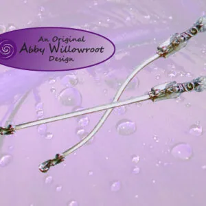 Three white wands with decorative beaded handles arranged on a purple background with water droplets and a purple Abby Willowroot Design label