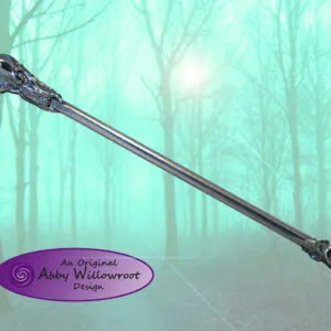 Dark wooden wand with ornate head and tip against misty forest backdrop