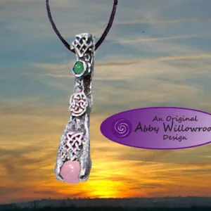 Silver filigree pendant with green and pink stones on dark cord against sunset sky