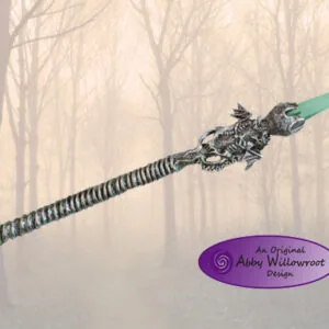 Ornate double-dragon wand with green crystal top and textured silver handle against misty forest background