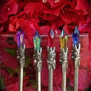 Five decorative wands with silver branch-textured handles and colored crystal tops in purple, green, yellow, and blue, displayed against red flowers
