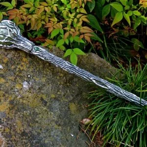Decorative wand with wrapped handle resting on lichen-covered stone beside autumn foliage