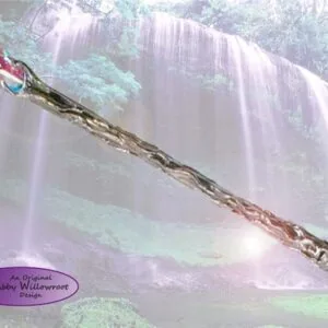 Decorative wand with colorful wrapped handle resting on a weathered branch against a misty waterfall and forest background