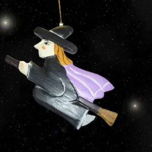 Ornament of a witch in black robes and wide-brimmed hat flying on a broomstick against a starry night sky