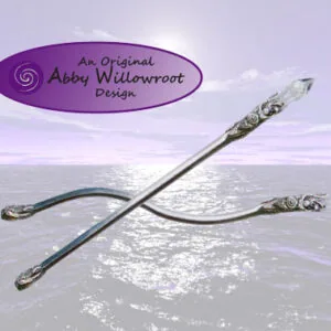 Curved silver wand with ornate handles displayed on sandy beach with ocean and sky backdrop