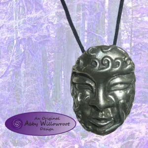 Cast metal mask pendant with stylized face features, hanging from black cord against purple textured background