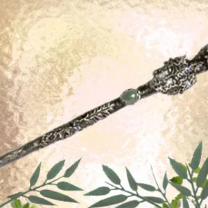 Ornate wand with dark patterned handle and pointed tip on textured beige surface with green foliage