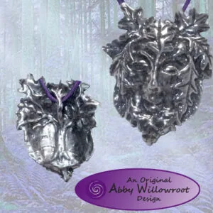 Two ornate silver green man face pendants with purple ribbons hanging against misty forest background