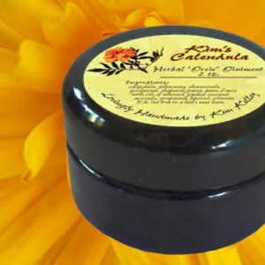 Black jar of herbal ointment with cream-colored label on yellow flower background
