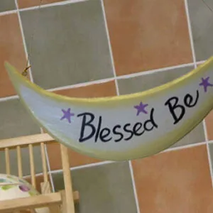 Blessed Be crescent moon plaque with purple stars hanging on tiled wall above wooden chair