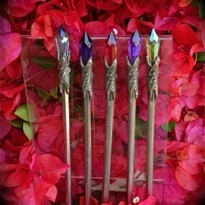 Five decorative wands with colored crystal tips arranged in a row against vibrant red and pink flowers