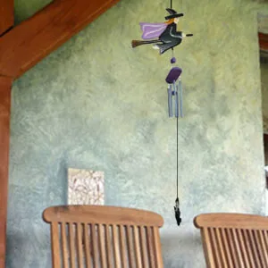Witch-themed wind chime with purple fabric and broomstick hanging above wooden chairs