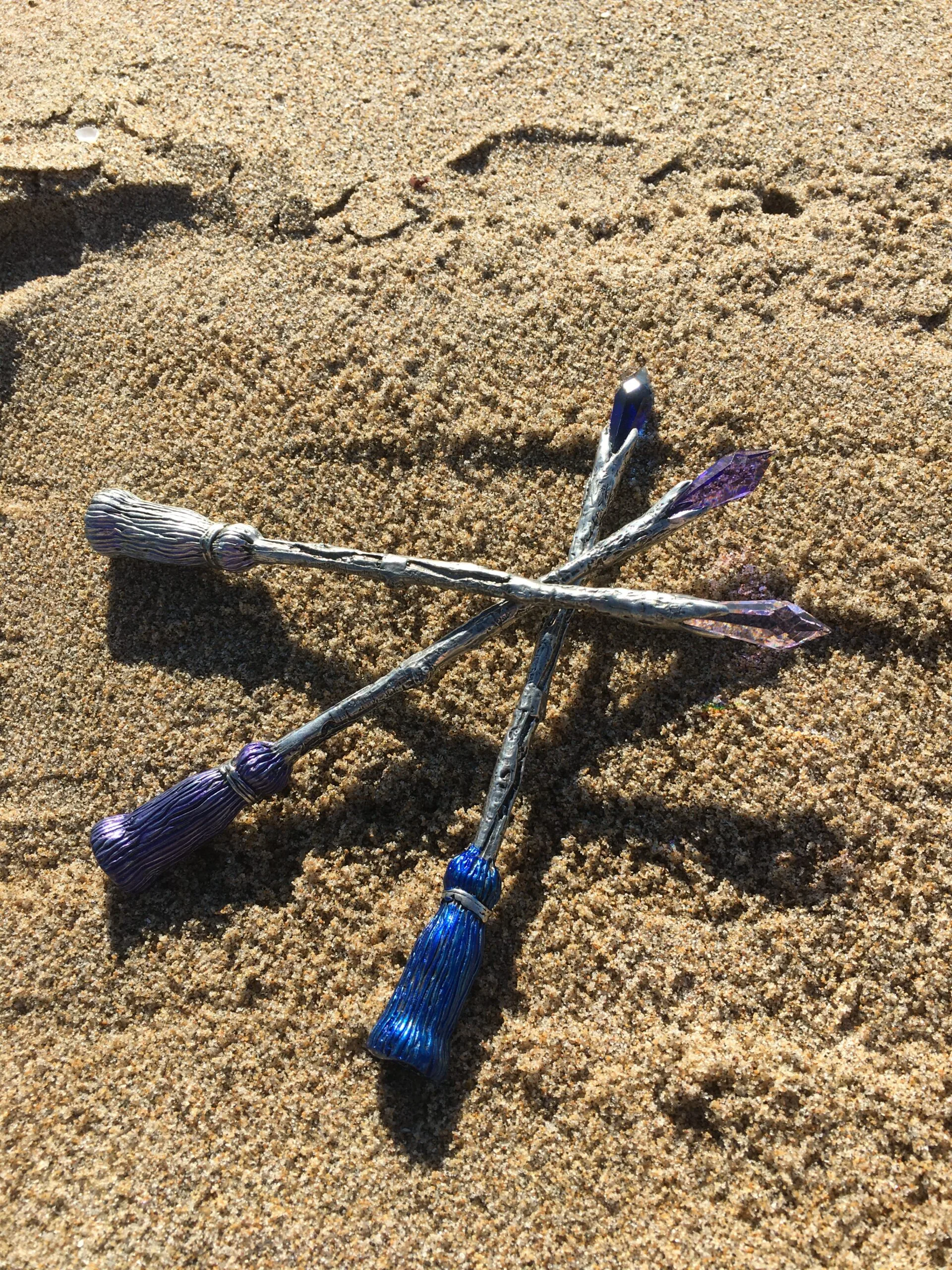 Four paintbrushes with blue bristles arranged in cross pattern on sandy beach surface