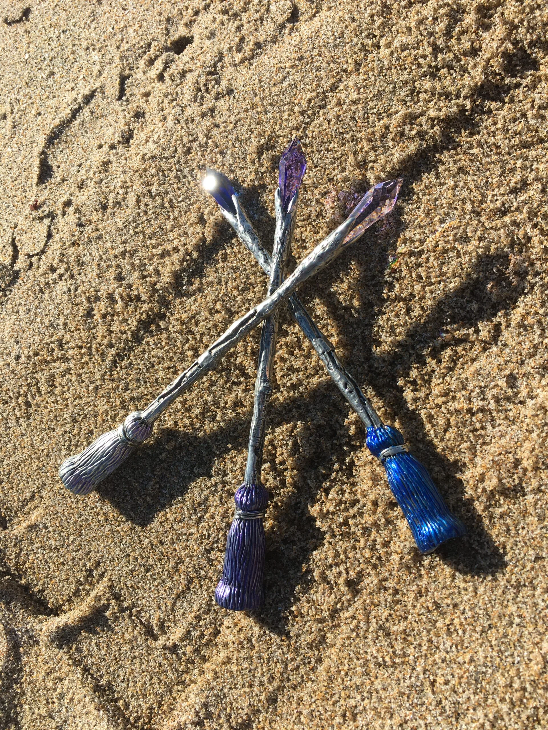 Three paint brushes with blue and purple bristles arranged on sandy beach surface