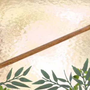 Wooden wand with ornate metal ends on textured gold background with green foliage