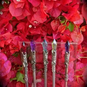 Five decorative wands with ornate silver handles and colored crystal tips displayed against vibrant red and pink bougainvillea flowers.