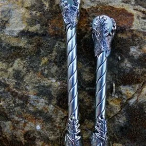 Two decorative wands with twisted silver shafts and ornate leaf-topped handles on weathered stone background