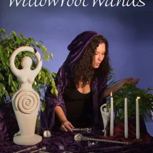 Woman with long dark hair wearing purple shawl sitting at table with spiral goddess figurine, white candles, and mystical items