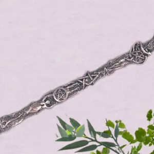 Silver decorative wand with pentacle and goddess designs on handle, sphere topper, displayed on pale background with green foliage.