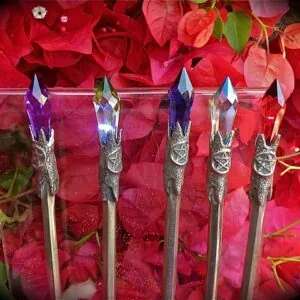 Five decorative wands with pointed crystal tops and ornate silver handles displayed against vibrant red and pink poinsettia flowers