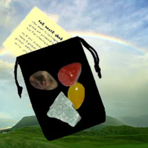 Black drawstring pouch containing stones, crystals, and natural objects displayed against a pastoral landscape with sky