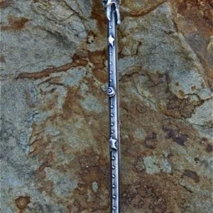 Silver and black wand with ornate handle and engraved shaft lying on textured stone surface