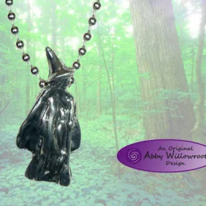 Black metal witch pendant hanging from ball chain against forest background