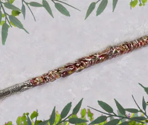 Wooden wand with copper wire wrapping and natural wood grain, surrounded by green foliage