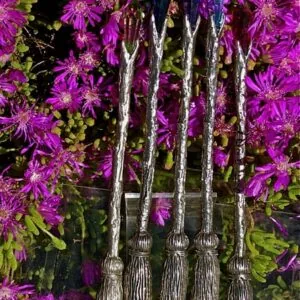 Five decorative broomstick wands with white-painted handles arranged in a fan pattern against vibrant magenta and green flowers